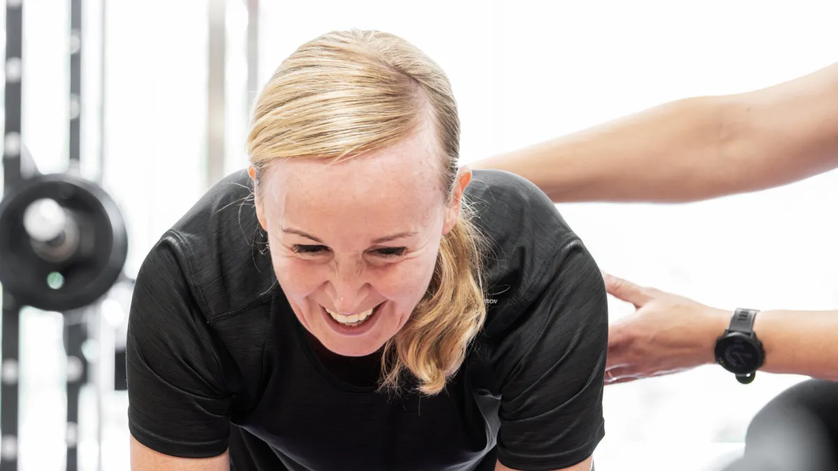 Klant traint lachend op een mat terwijl Miriam haar met een hand op de rug bijstuurt